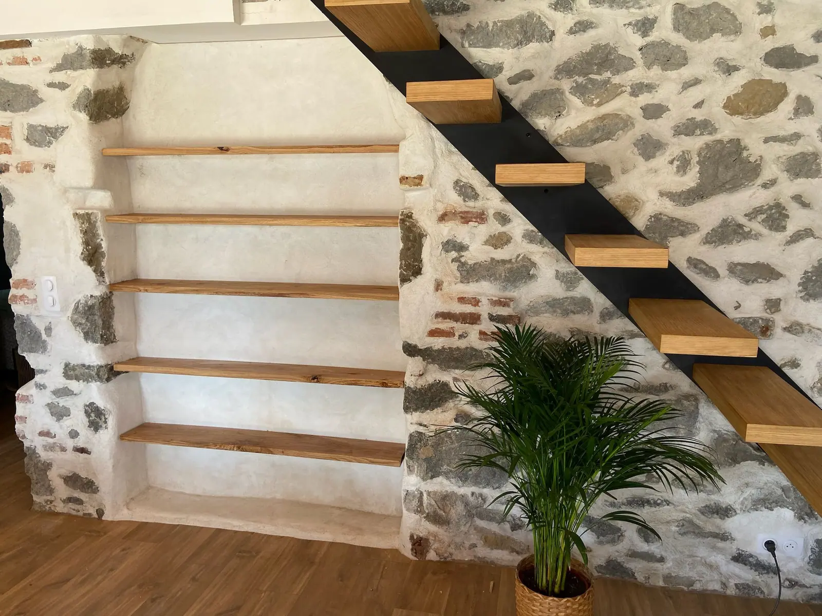 Étagères sur mesure dans une niche de pierre, à côté d’un escalier en acier noir et marches en bois